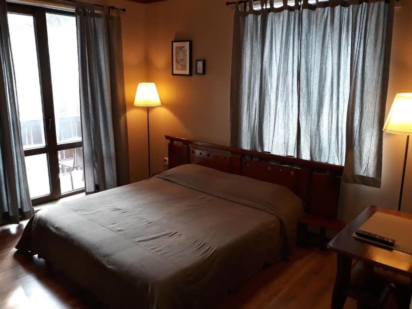 Cozy hotel bedroom with large window, wooden headboard, and illuminated floor lamps.