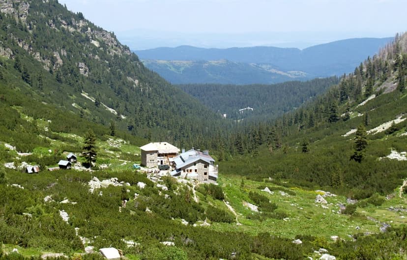 Stone mountain hut nestled in a green valley surrounded by pine-covered slopes, Malyovitsa.