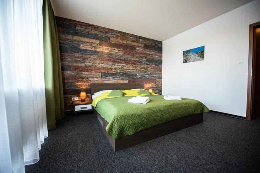 Bedroom with green bedding, wood accent wall, and sheer white curtains