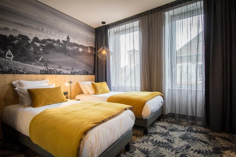 Twin hotel room with yellow bedding, wood headboard, and black and white village mural.