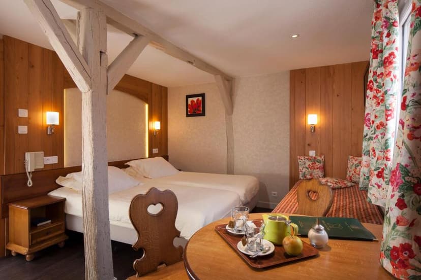 Hotel room with twin beds, wooden beams, and a table set for tea near floral curtains.