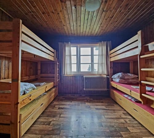 Wooden bunk beds in a rustic mountain hut room with a window view.