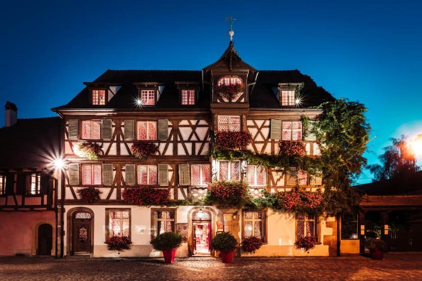Half-timbered hotel illuminated at night with red flower boxes on a cobblestone street.