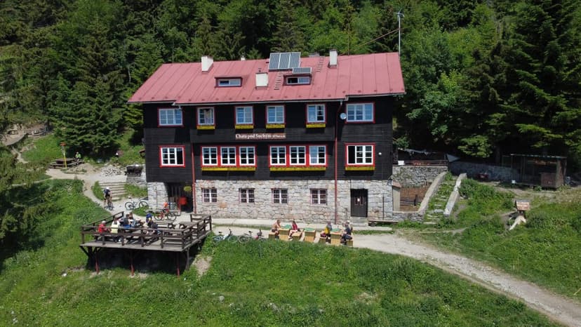Chata pod Suchým mountain hut with wooden deck, cyclists, and surrounding forest.