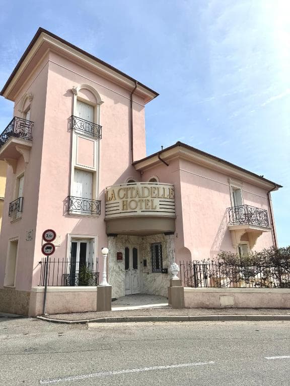 Hotel La Citadelle building with pink facade and ornate iron balconies under blue sky