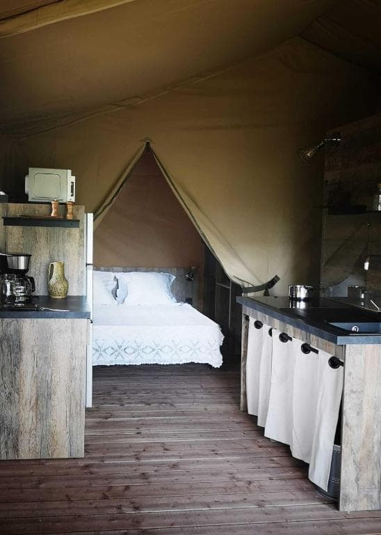 Interior of a glamping tent showing a bed, kitchenette, and wooden floor.
