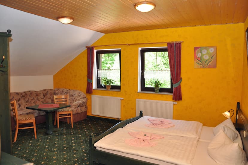 Guest room with yellow walls, wooden ceiling, double bed, and seating area at Hubertushaus.