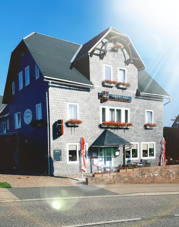 Hotel Restaurant Oberland building with gray shingle siding and flower boxes under blue sky.