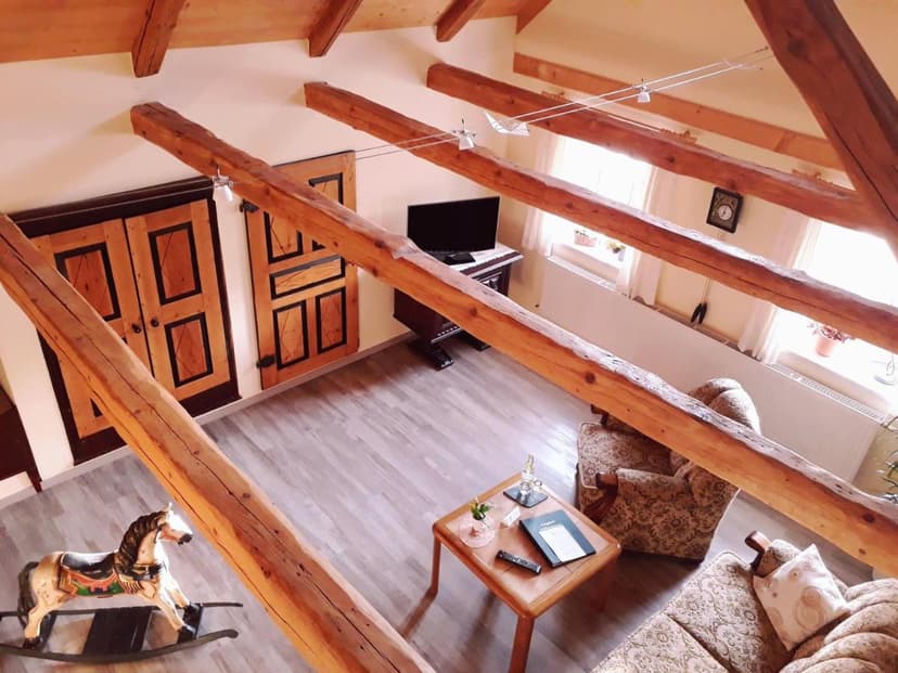 Attic hotel room with exposed wooden beams, rocking horse, and patterned seating in Antikhotel Steinbacher Hof.