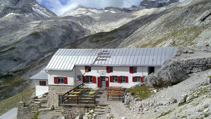 Knorrhütte mountain refuge with outdoor seating against a backdrop of rocky, snow-dusted alpine peaks.