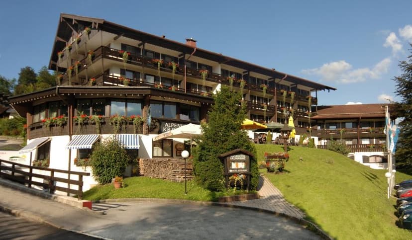 Alpenhotel Kronprinz building with balconies, flower boxes, and outdoor seating on a grassy slope.