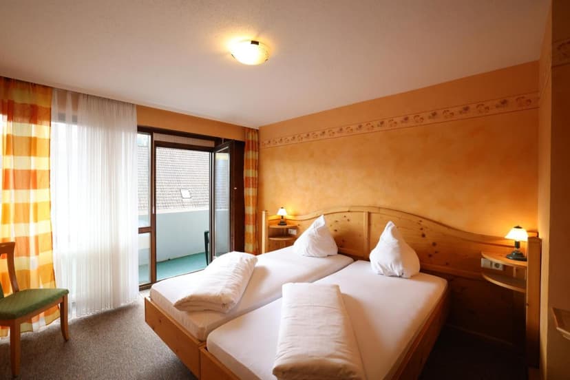 Twin beds with white linens in a room featuring orange walls and balcony access at Hotel Gasthof Hirschen.