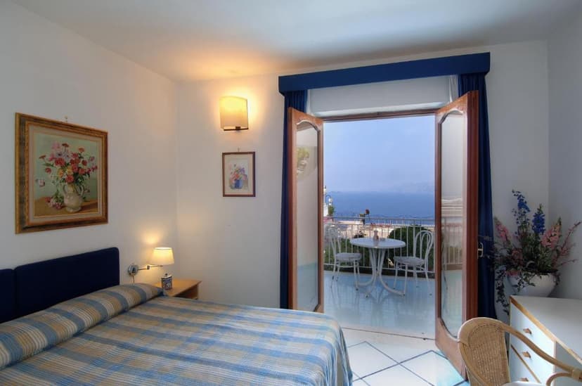 Hotel room with blue plaid bedspread opening to balcony overlooking the sea.
