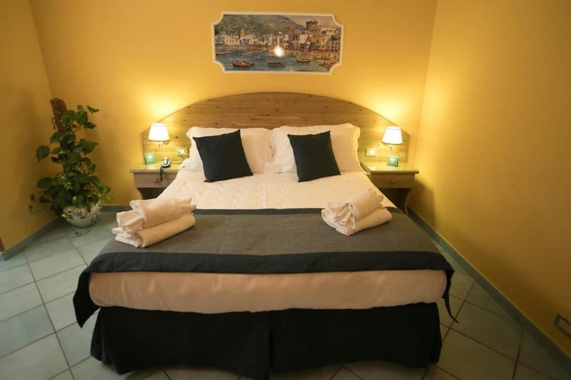 Hotel bedroom with yellow walls, wooden headboard, white bedding, and coastal artwork.