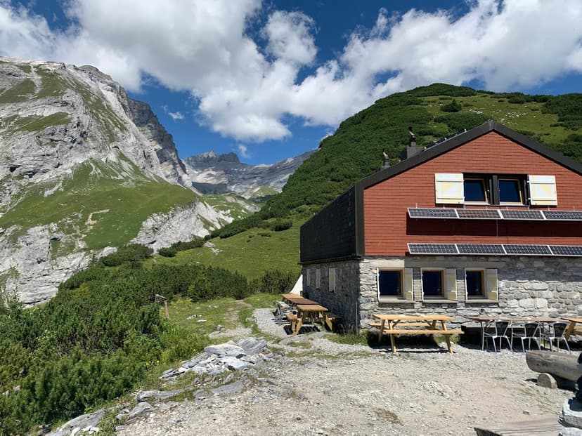 Ringelspitzhütte mountain hut with picnic tables below steep, grassy, rocky peaks.