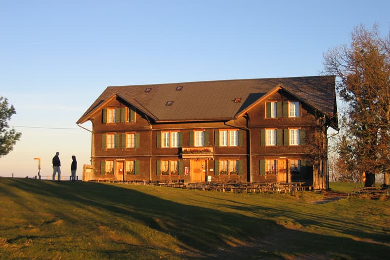 Berghotel Napf wooden lodge with green shutters on grassy hillside at sunset