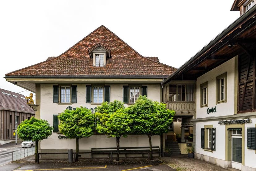 Hotel building with terracotta roof, green trees, and a golden lion sign in front of a street.