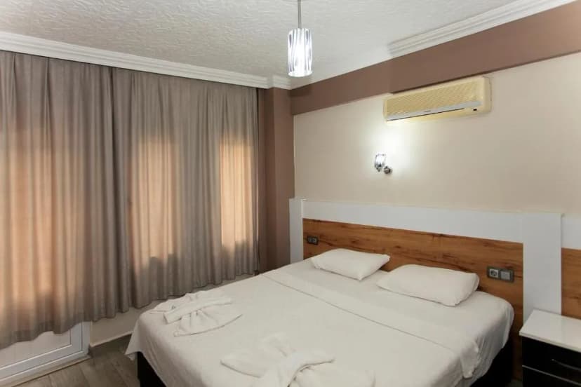 Double bed with white linens, air conditioner, and sheer curtains in a hotel room.