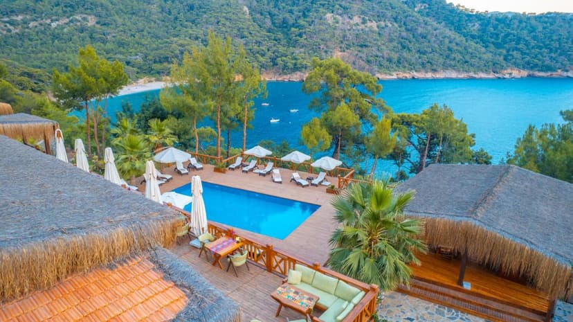 Resort pool deck with thatched roofs overlooking turquoise bay and forested hillsides