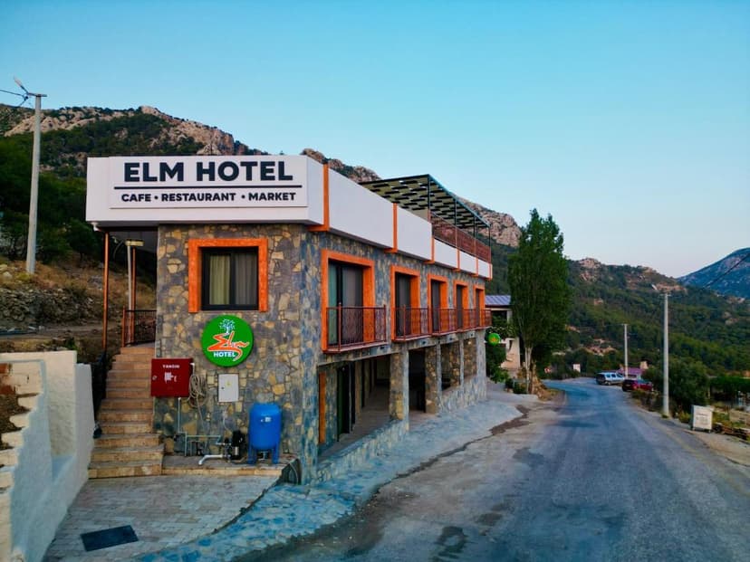 Elm Hotel with cafe, restaurant, and market sign, set against lush green mountains.