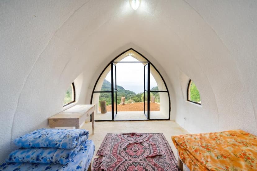 Interior of white dome room with arched door opening to green mountainside view
