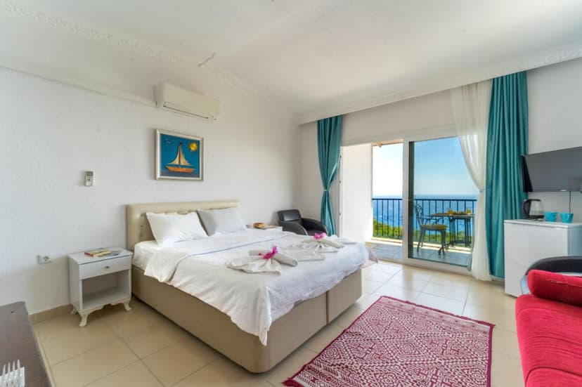 Bright hotel room with white bedding, sailboat art, and balcony overlooking the blue sea.