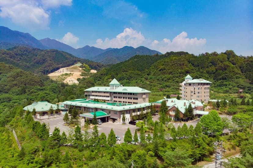 Resort complex with green roofs nestled in lush green mountains under a blue sky, Kisoji area.