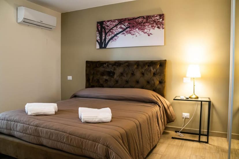 Bedroom with brown bed, tufted headboard, wall art of pink blossoms, and air conditioner