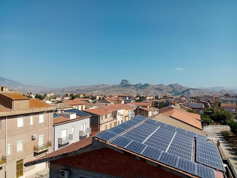 Rooftops with solar panels overlooking a town nestled against arid, rocky mountains under a clear blue sky.
