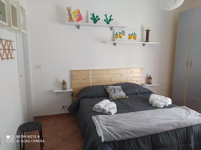 Bedroom with wooden headboard, dark bedding, white towels, and decorative shelves with lemons and cacti art.