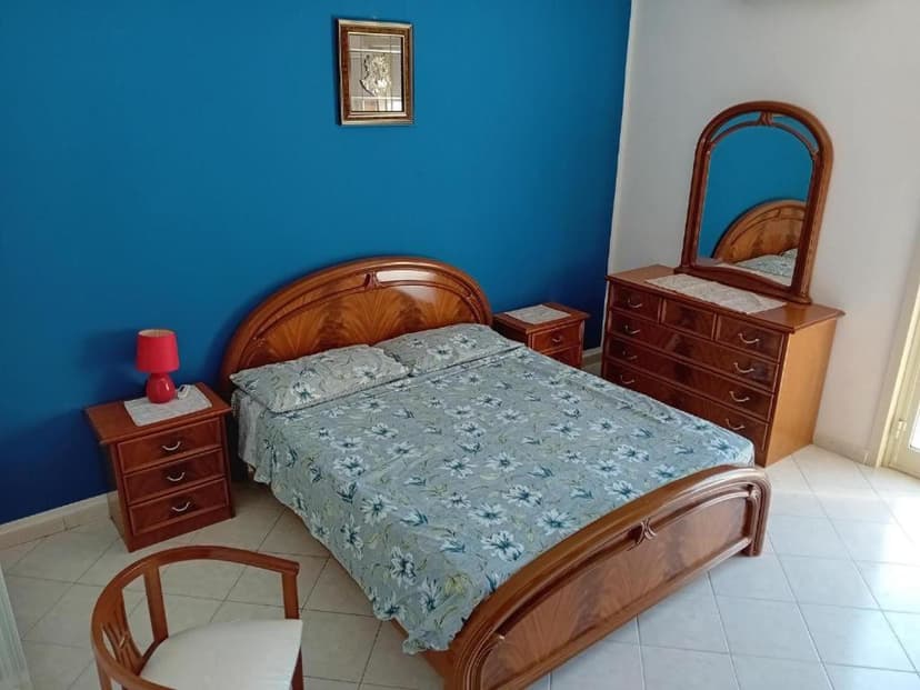 Bedroom with wooden bed, blue wall, and dresser with mirror, likely in Scozzaro.