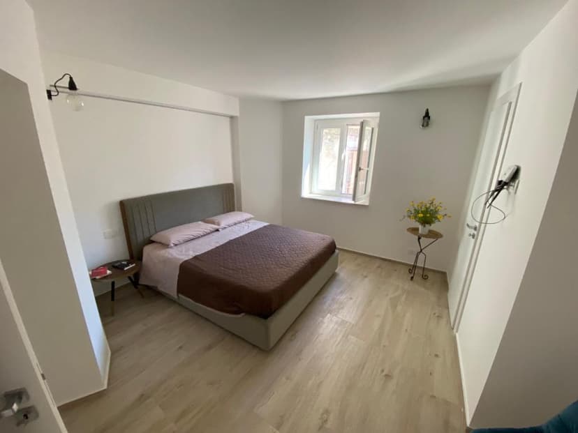 Bedroom with double bed, light wood floor, and open window in a room with white walls