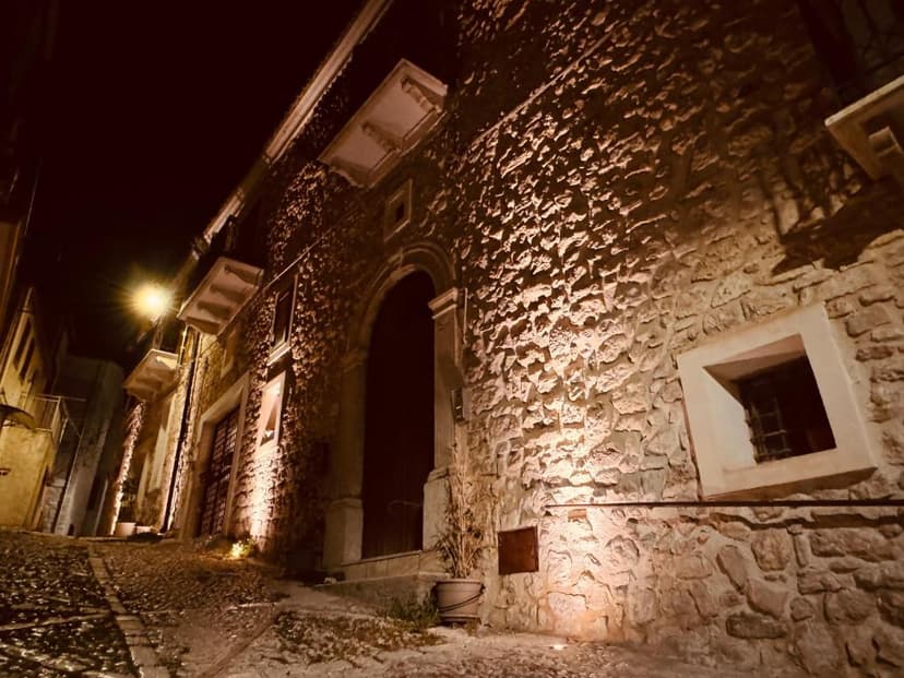 Stone building facade illuminated at night on a cobblestone street in a historic town.
