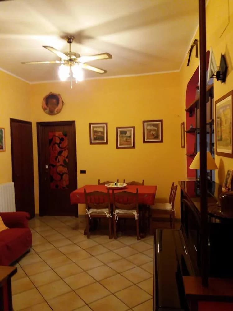 Living room with yellow walls, tiled floor, ceiling fan, and dining table with red cloth.