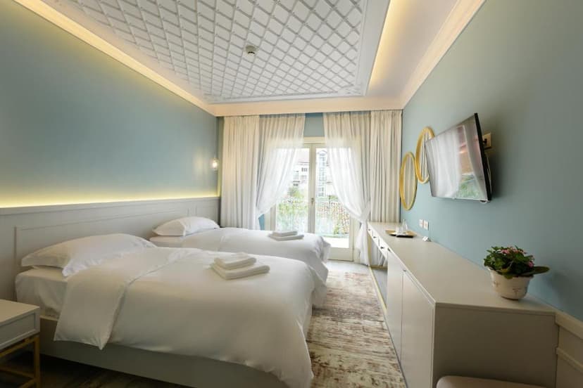Twin beds in a boutique hotel room with light blue walls and ornate ceiling.