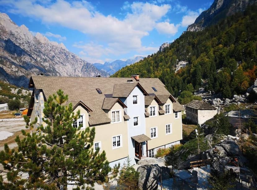 Guesthouse in Valbona surrounded by steep, rocky mountains and green forest.