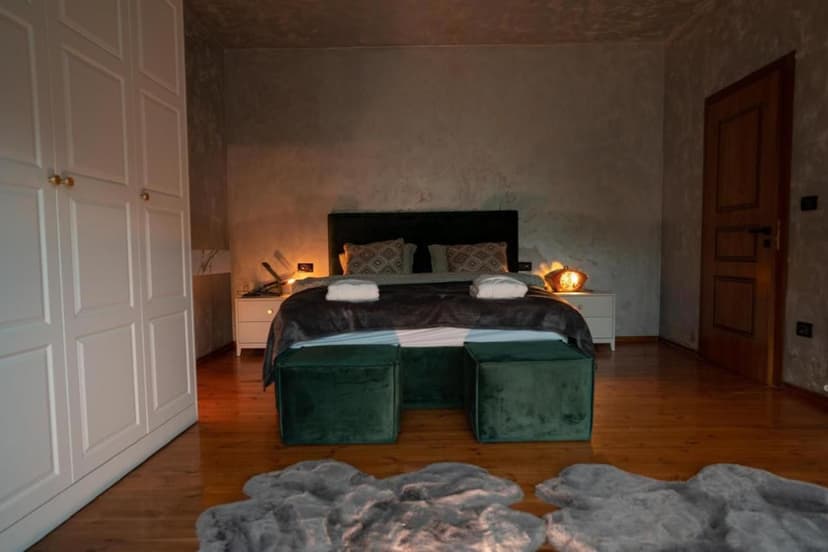 Bedroom with dark walls, white wardrobe, wood floor, and green velvet ottomans at Zeneli Alpin Chalet.