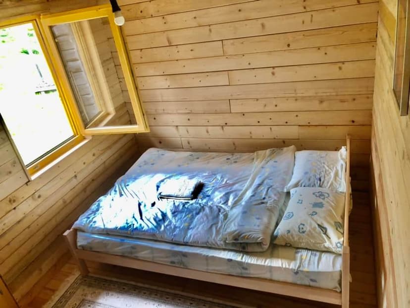 Wooden cabin bedroom with a double bed, light wood walls, and an open window.