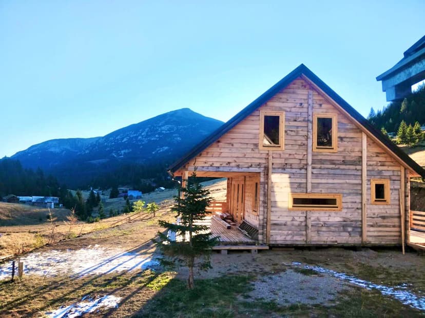 Wooden chalet under a large mountain peak with patches of snow on the ground