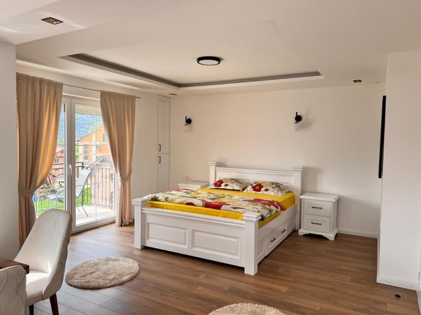 Bright bedroom with white furniture, wood floor, and balcony view of green mountains.