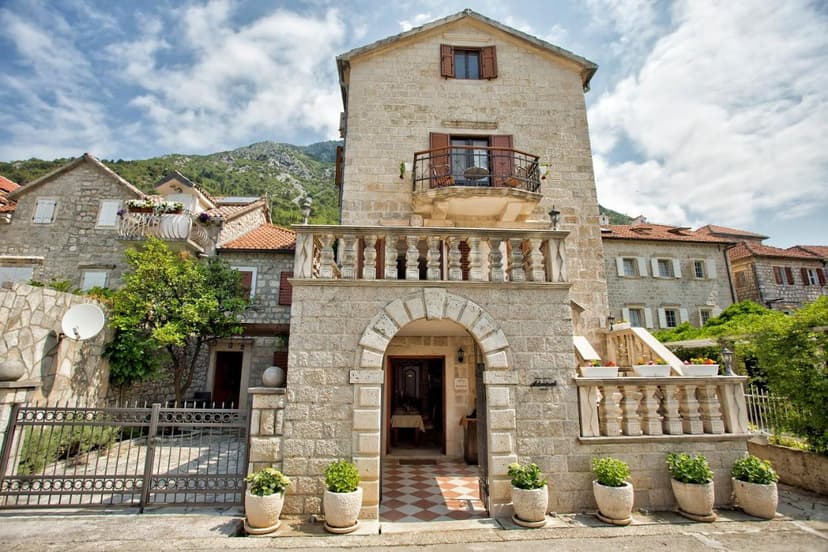 Stone hotel entrance with arched doorway, balconies, and mountain backdrop.