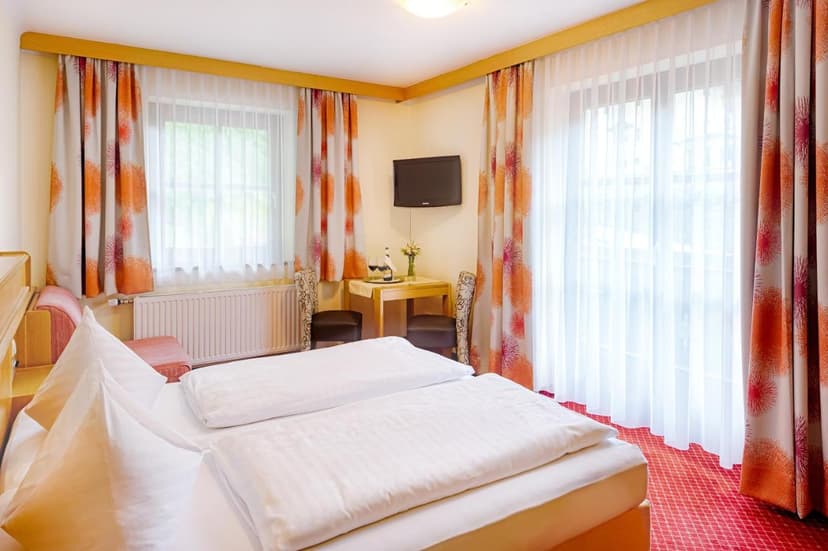 Double bed with white linens in a hotel room at Landhotel Almrösl im Großarltal.