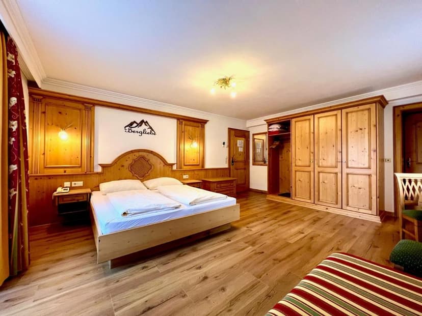 Gasthof Bacher guest room with wooden paneling, large bed, and pine wardrobe
