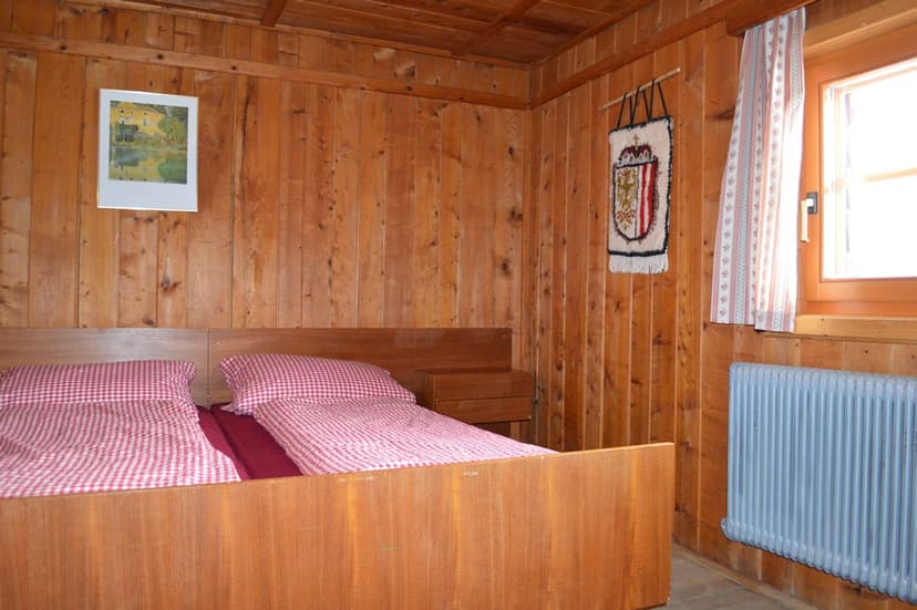 Wooden room interior with twin beds, red gingham bedding, and a wall tapestry at Neue Bonner Hütte.