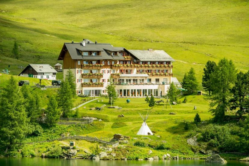 Hotel Falkertsee by alpine lake with green meadows and surrounding pine trees