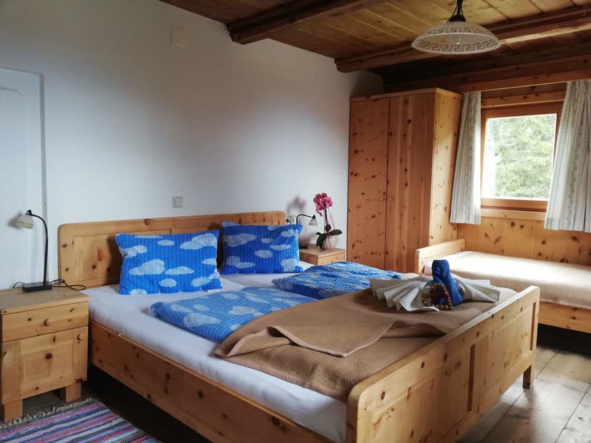 Wooden bedroom with pine furniture, blue cloud bedding, and a window view of green trees.