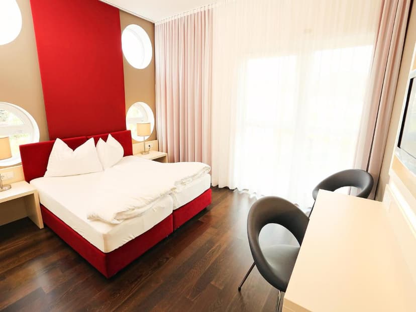 Hotel room with red headboard, white bedding, dark wood floor, and circular windows.