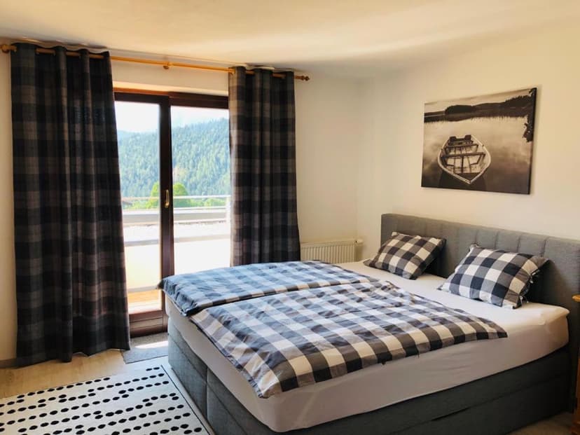 Bedroom with plaid bedding, balcony view of forested mountains, Bergkristallhaus.