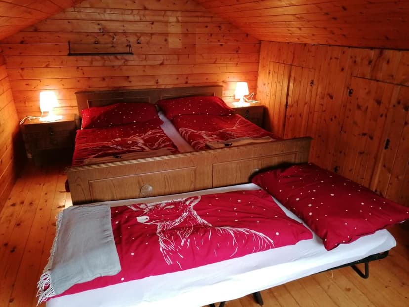 Cozy wooden attic room with double bed featuring red deer-themed bedding in Stoderhütte.