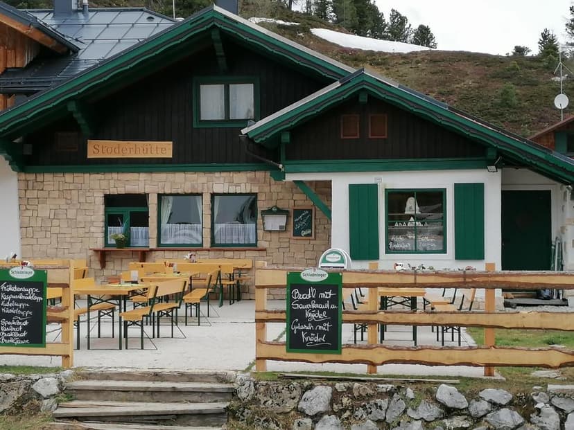 Stoderhütte mountain restaurant with outdoor seating and snow patches on the hill.